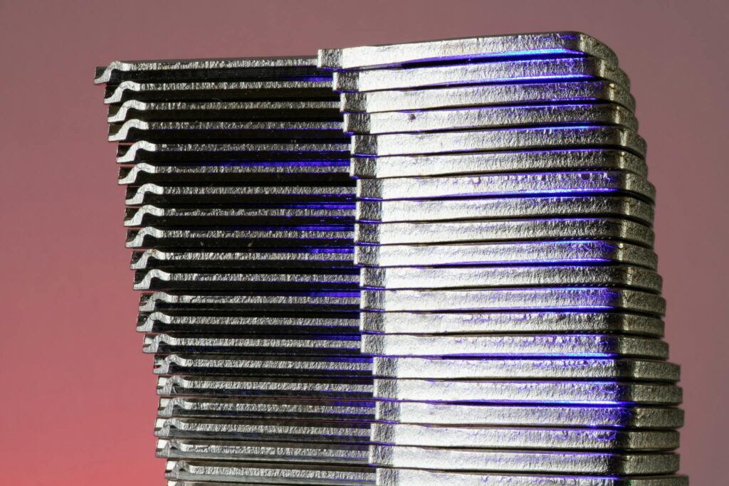 Close-up of stacked metallic sheets reflecting purple light against a gradient background.