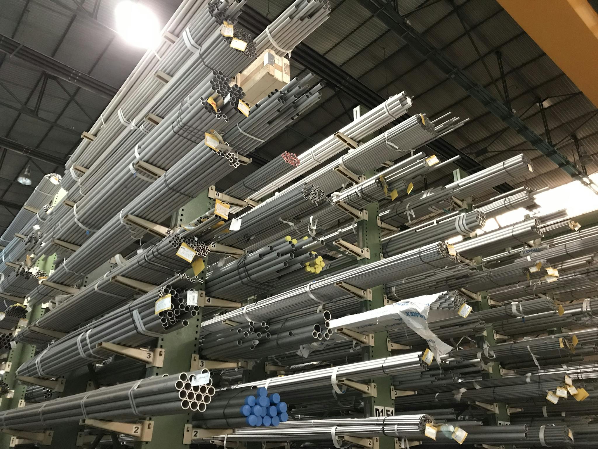 Wide view of metal pipes stacked in an industrial warehouse, emphasizing storage and organization.